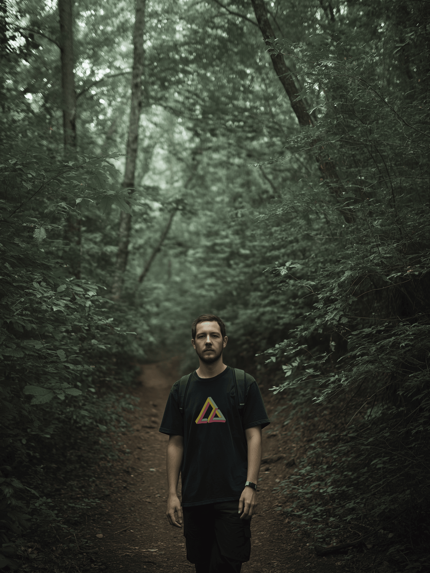 Male hiking on trail wearing black shirt with impossible geometry design triangle graphic in yellow, red, and green – Wanderluz