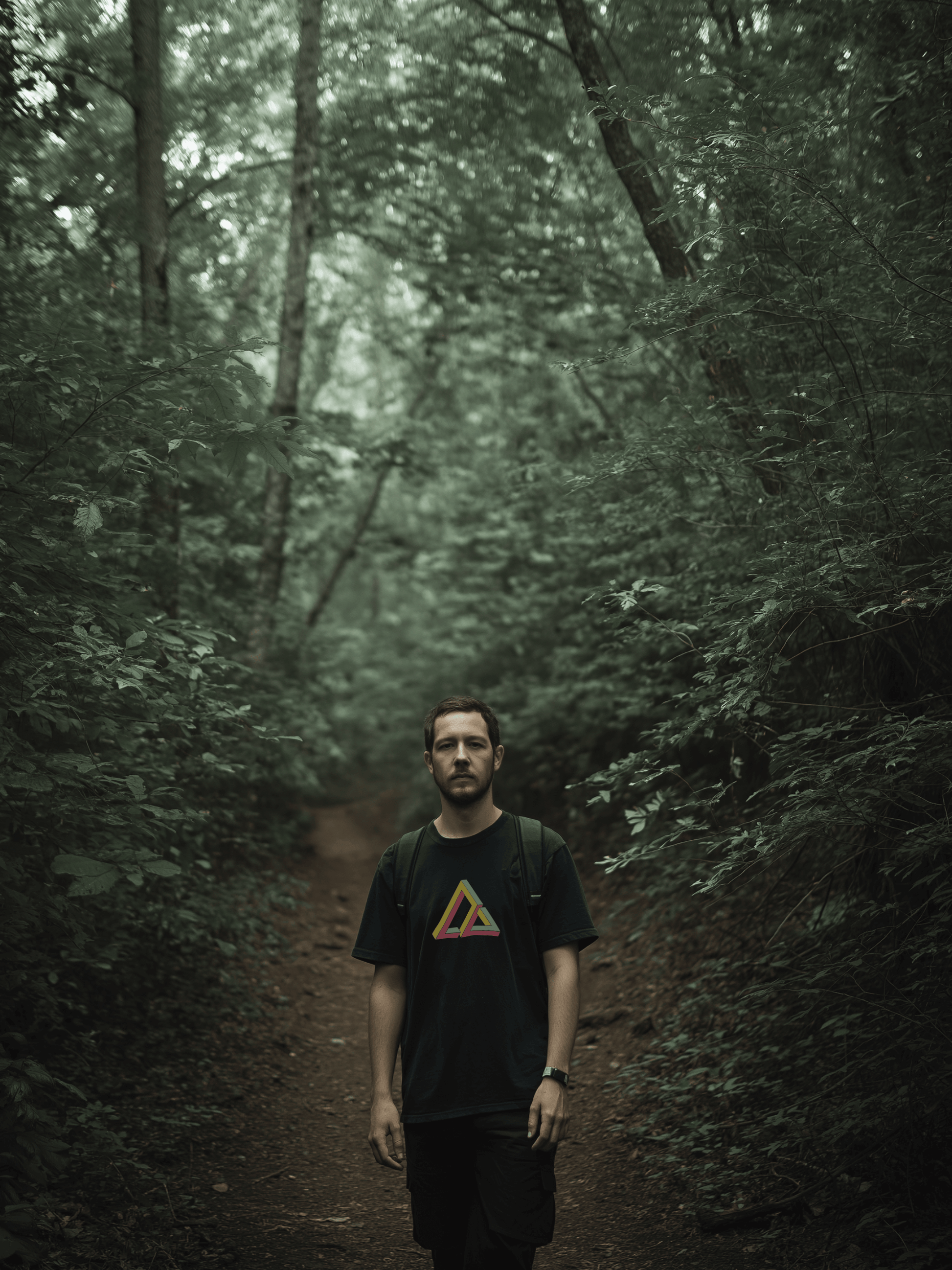 Male hiking on trail wearing black shirt with impossible geometry design triangle graphic in yellow, red, and green – Wanderluz